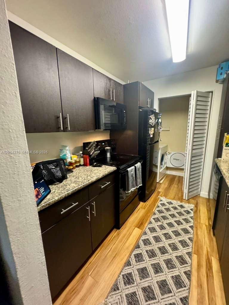 A galley kitchen features dark wood cabinets, black appliances, granite countertops, and wood-look flooring — 3979 NW 87th Ave # 3979, Sunrise FL 33351, SUNRISE, FL