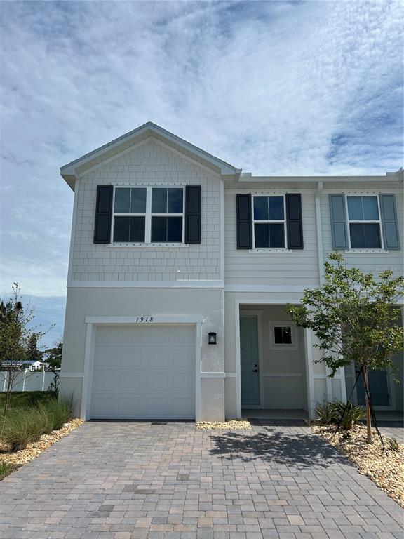 A two-story townhouse exterior features a single-car garage, light siding, and a paver driveway — 1918 KENDALL POINTE PLACE, MELBOURNE, FL