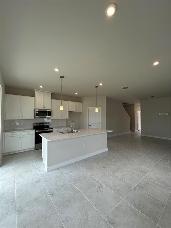 A kitchen features white cabinets, a central island with a sink, and light-colored tile flooring — 1918 KENDALL POINTE PLACE, MELBOURNE, FL