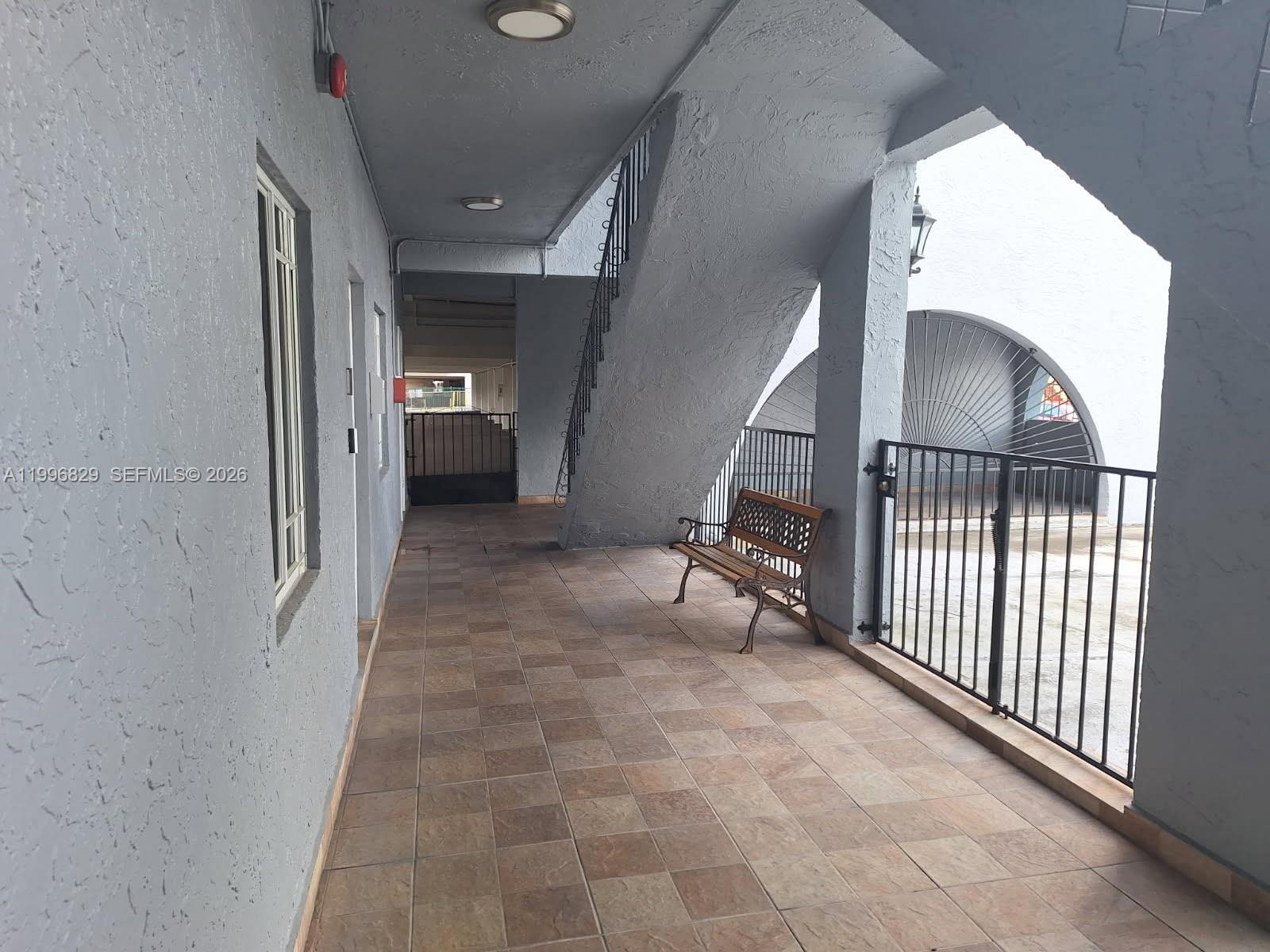 An outdoor tiled walkway features a wooden bench, metal railings, and a staircase — 1300 W 53rd St # 35, Hialeah FL 33012, HIALEAH, FL