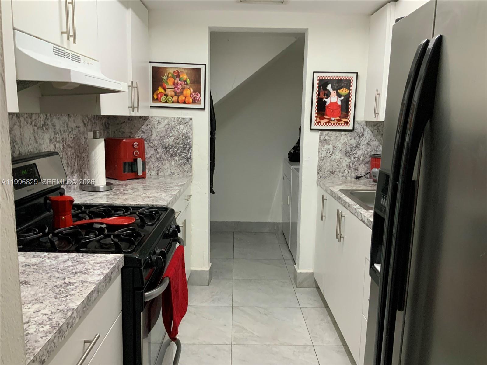 A galley kitchen features white cabinets, marble-patterned countertops, and stainless steel appliances — 1300 W 53rd St # 35, Hialeah FL 33012, HIALEAH, FL