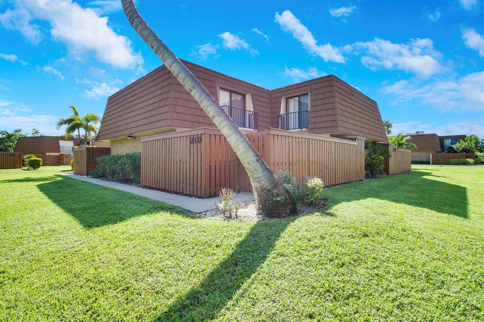 A two-story brown building with a fenced patio and a palm tree in the foreground — 3900 County Line Road # 21d, Tequesta FL 33469, TEQUESTA, FL