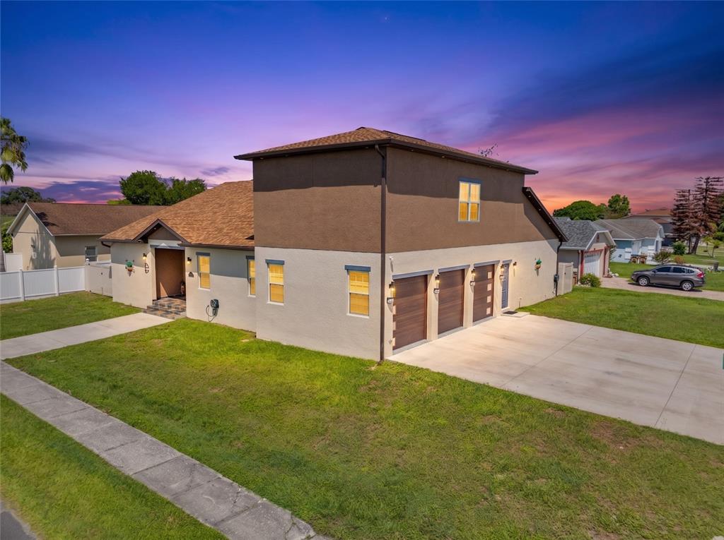 A two-story house with a tan stucco exterior and a three-car garage at sunset — 501 ROYAL PALM DRIVE, KISSIMMEE, FL