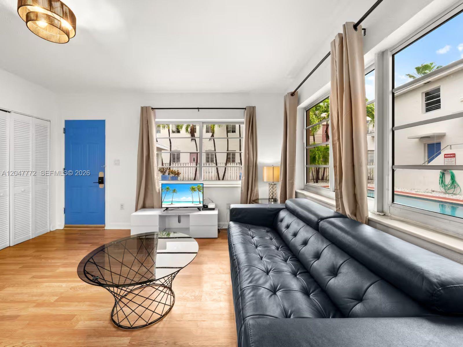 A living room features a dark leather sofa, glass coffee table, and a blue door — 1032 Michigan Ave # C, Miami Beach FL 33139, MIAMI BEACH, FL
