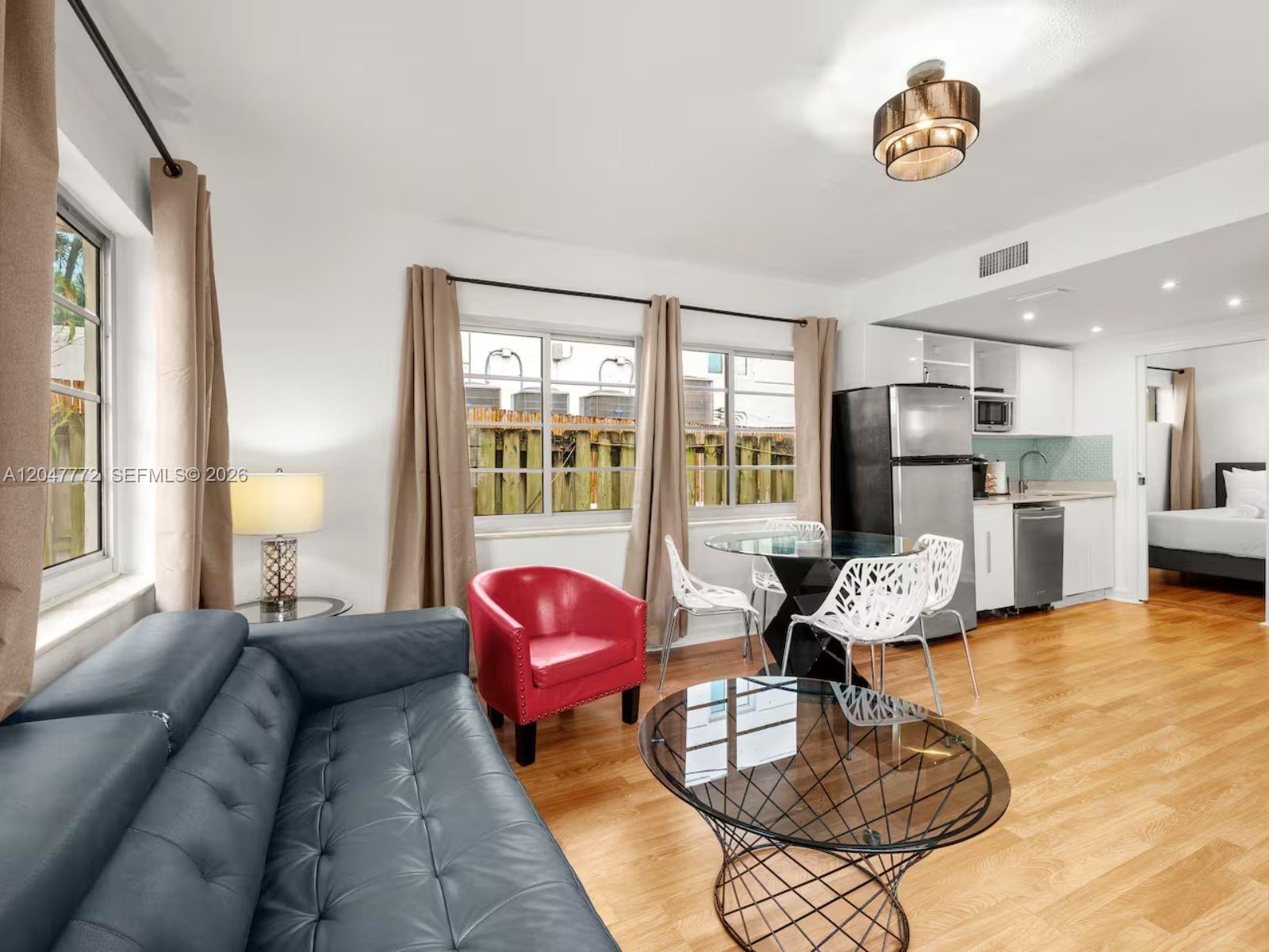 A living room with a blue sofa, red armchair, glass coffee table, and adjacent kitchen — 1032 Michigan Ave # C, Miami Beach FL 33139, MIAMI BEACH, FL