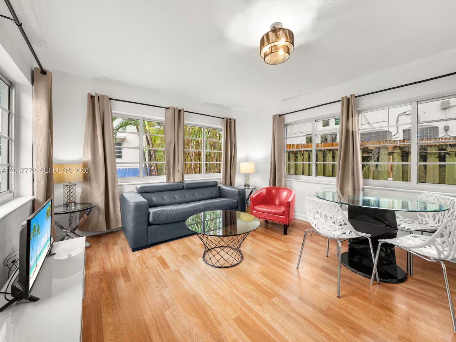 A living and dining area features hardwood floors, a grey sofa, and a glass table — 1032 Michigan Ave # C, Miami Beach FL 33139, MIAMI BEACH, FL