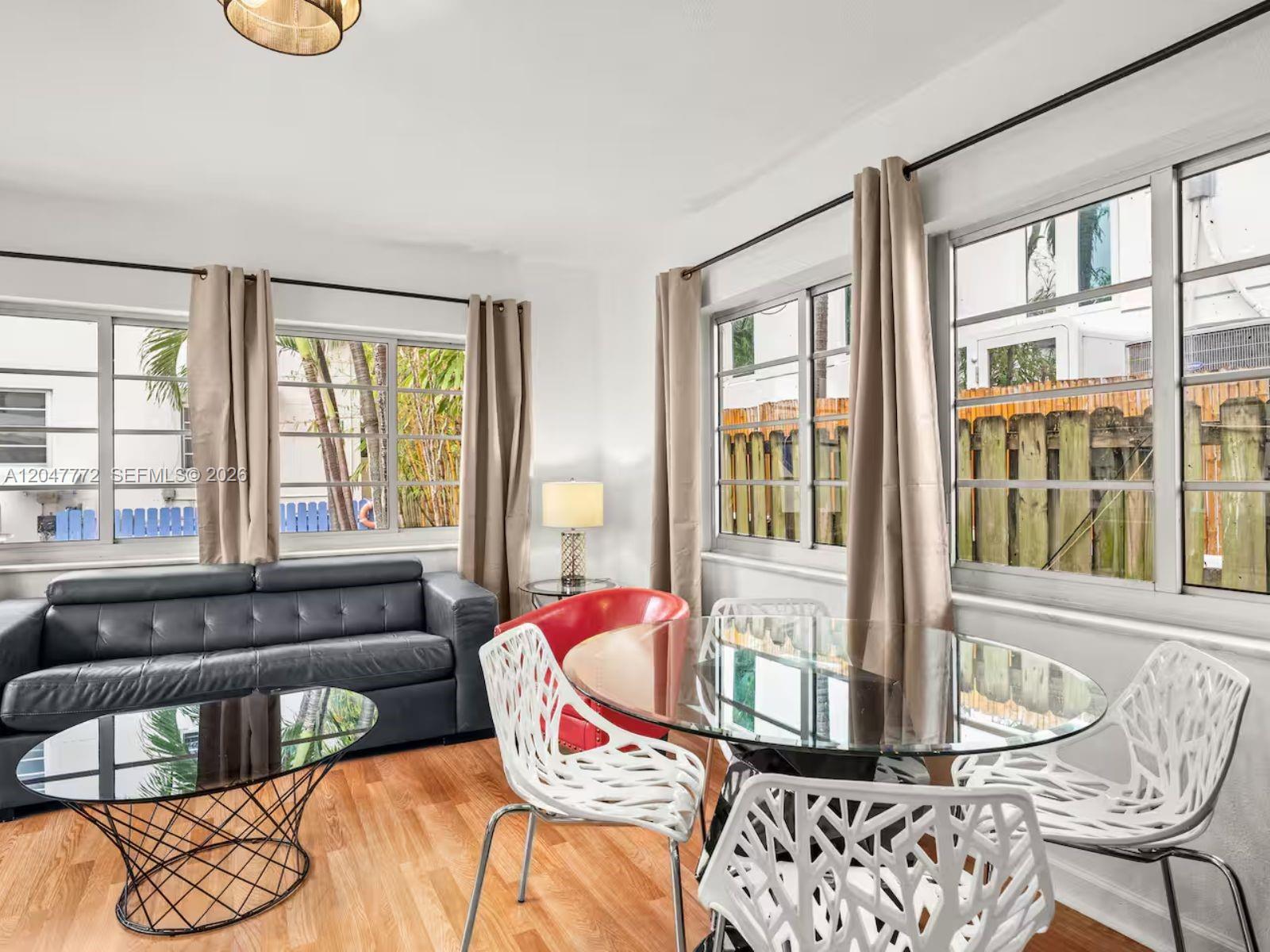 A living and dining area features a black leather sofa, glass tables, and white chairs — 1032 Michigan Ave # C, Miami Beach FL 33139, MIAMI BEACH, FL