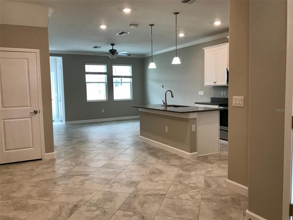A kitchen with a granite island, white cabinets, and tile flooring opens to a living area — 18672 NOBLE CASPIAN DRIVE, LUTZ, FL
