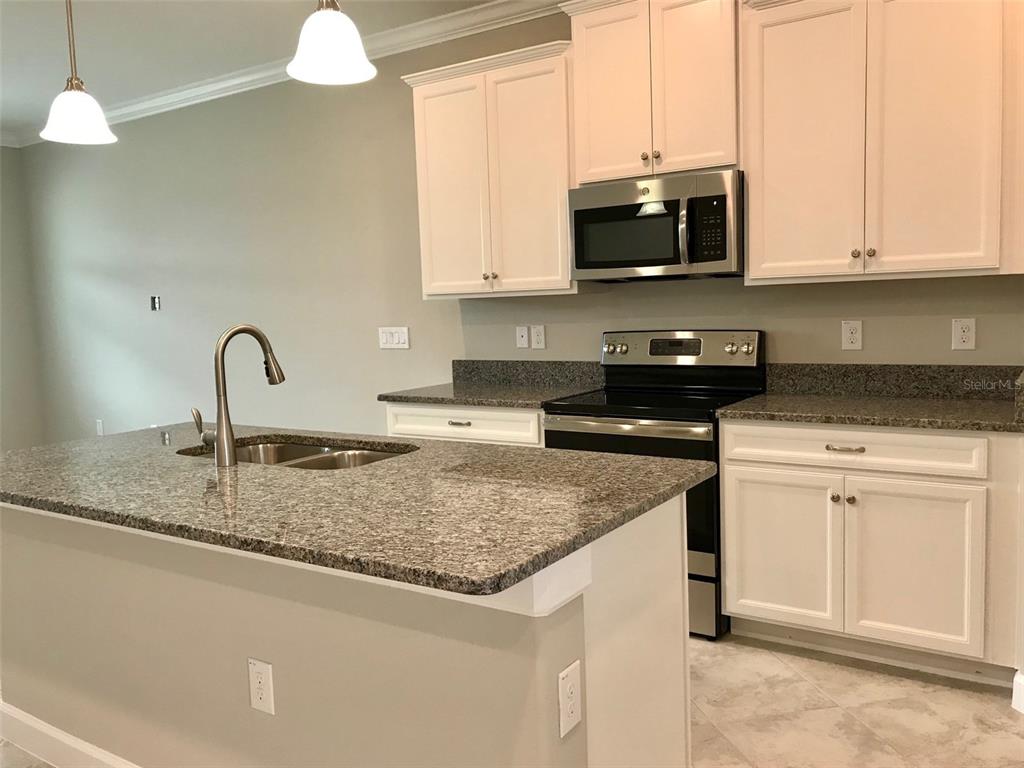 A kitchen features white cabinets, granite countertops, a center island with a sink, and appliances — 18672 NOBLE CASPIAN DRIVE, LUTZ, FL