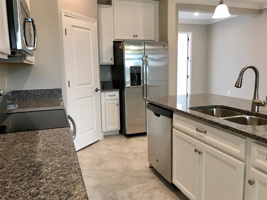 A kitchen features white cabinets, granite countertops, stainless steel appliances, and tile flooring — 18672 NOBLE CASPIAN DRIVE, LUTZ, FL