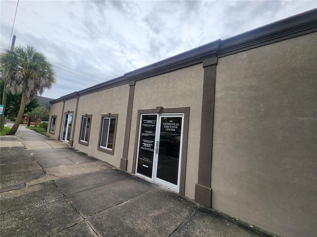 A tan commercial building exterior features a glass entrance door and several windows along the sidewalk — 309 NE 1ST STREET, GAINESVILLE, FL
