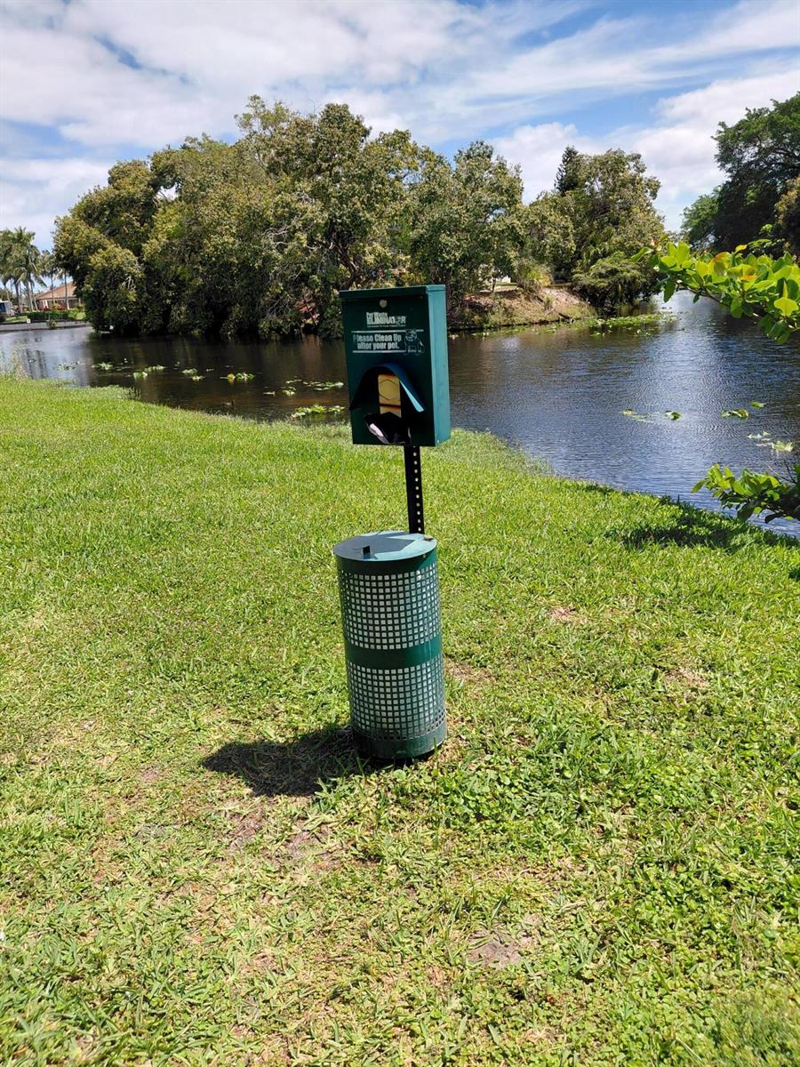 A green pet waste station stands on a grassy lawn beside a pond — 2403 S Waterside Drive # 2403, Lake Worth FL 33461, LAKE WORTH, FL