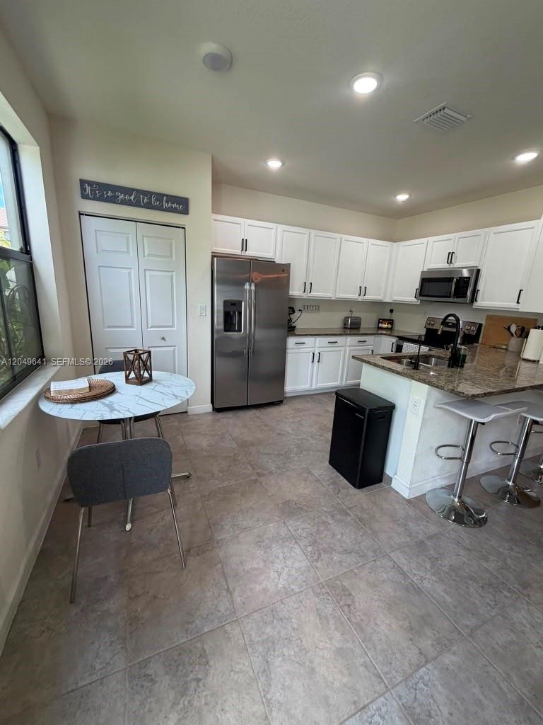 A kitchen features white cabinets, stainless steel appliances, granite countertops, and a small dining area — 3409 W 104th Ter, Hialeah FL 33018, HIALEAH, FL