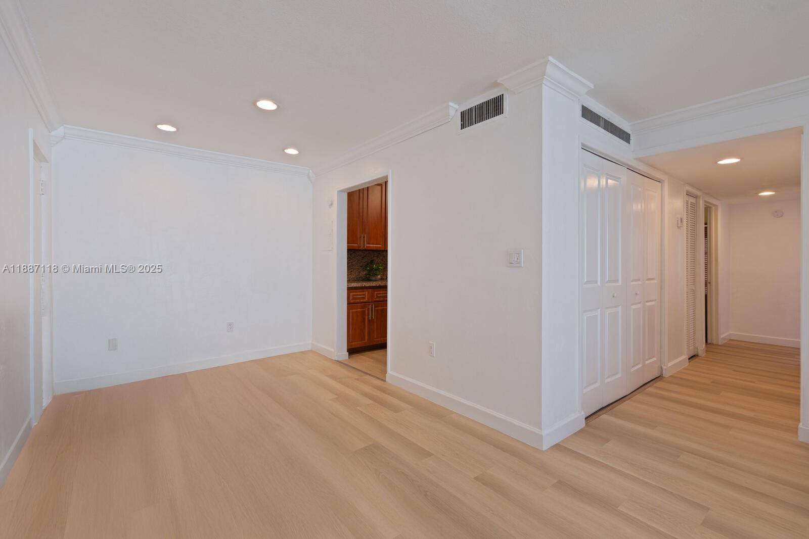 An empty room with light wood flooring, white walls, recessed lighting, and a kitchen doorway — 10816 N Kendall Dr # R16, Miami FL 33176, MIAMI, FL