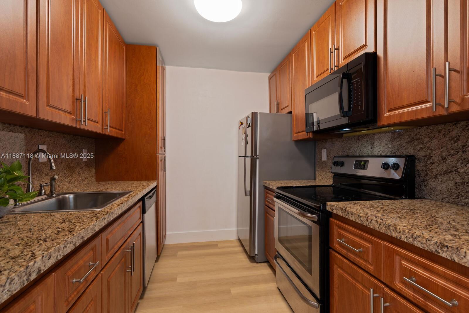 A galley kitchen features wood cabinets, granite countertops, and stainless steel appliances — 10816 N Kendall Dr # R16, Miami FL 33176, MIAMI, FL