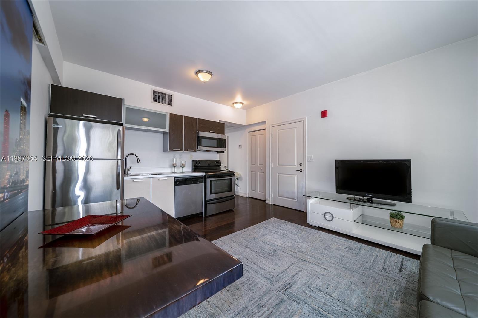 A kitchen and living area feature stainless steel appliances, dark cabinetry, and a glass television stand — 601 11th St # 206, Miami Beach FL 33139, MIAMI BEACH, FL