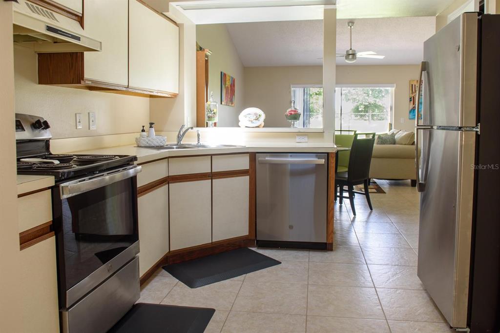 A kitchen with stainless steel appliances, off-white cabinetry, and tile flooring overlooks a living area — 13329 LAVER LANE, ORLANDO, FL