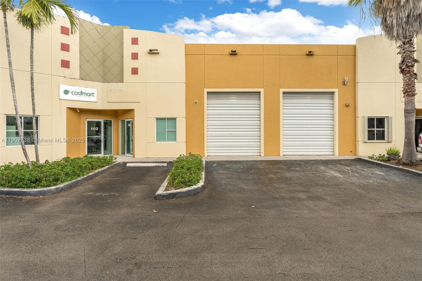 An exterior view of a commercial building featuring two roll-up doors and a pedestrian entrance — 9450 NW 58th St # 3, Doral FL 33178, DORAL, FL