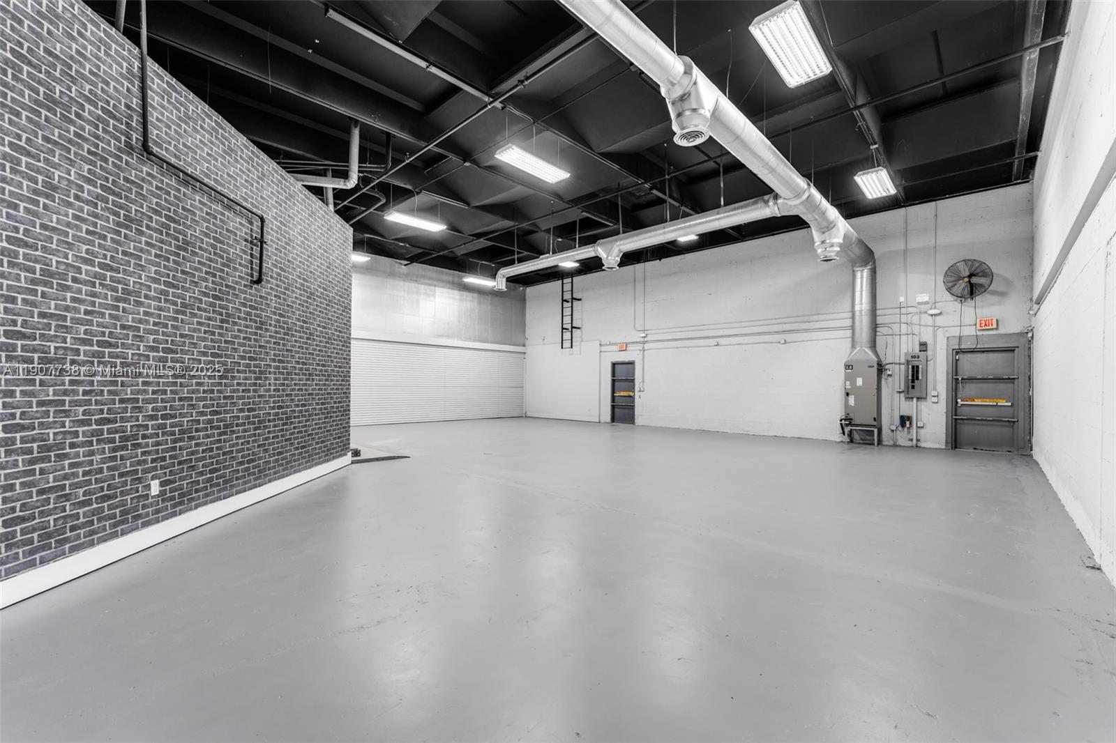 An empty industrial warehouse space features a brick accent wall, concrete floors, and exposed ductwork — 9450 NW 58th St # 3, Doral FL 33178, DORAL, FL