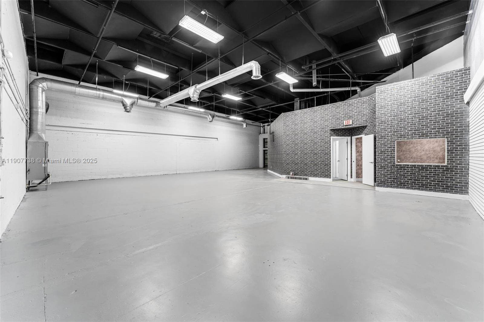This industrial space features a high ceiling, exposed ductwork, concrete floors, and a brick wall — 9450 NW 58th St # 3, Doral FL 33178, DORAL, FL