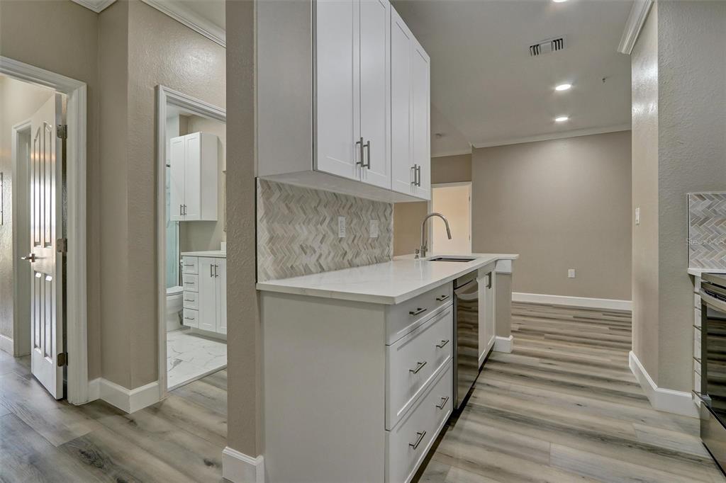 A kitchen with white cabinets, light countertops, and wood-look flooring, with a bathroom visible nearby — 5000 CULBREATH KEY WAY UNIT 4-306, TAMPA, FL