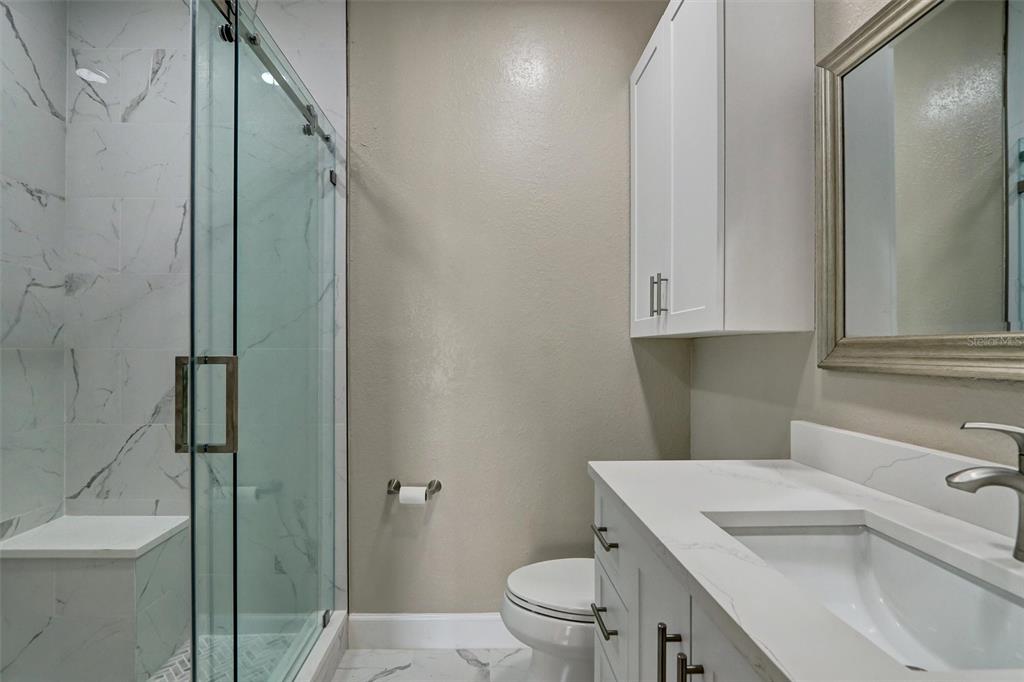A bathroom features a glass-enclosed shower, a white vanity with marble countertop, and a toilet — 5000 CULBREATH KEY WAY UNIT 4-306, TAMPA, FL