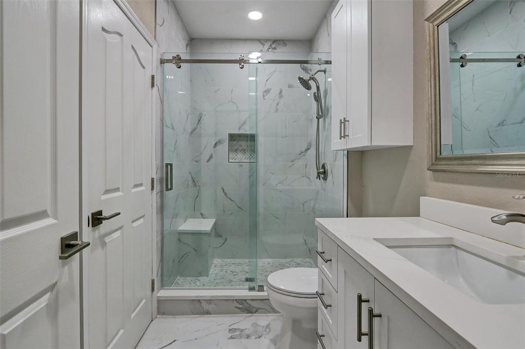 A modern bathroom features a marble-tiled walk-in shower, white vanity, and a toilet — 5000 CULBREATH KEY WAY UNIT 4-306, TAMPA, FL