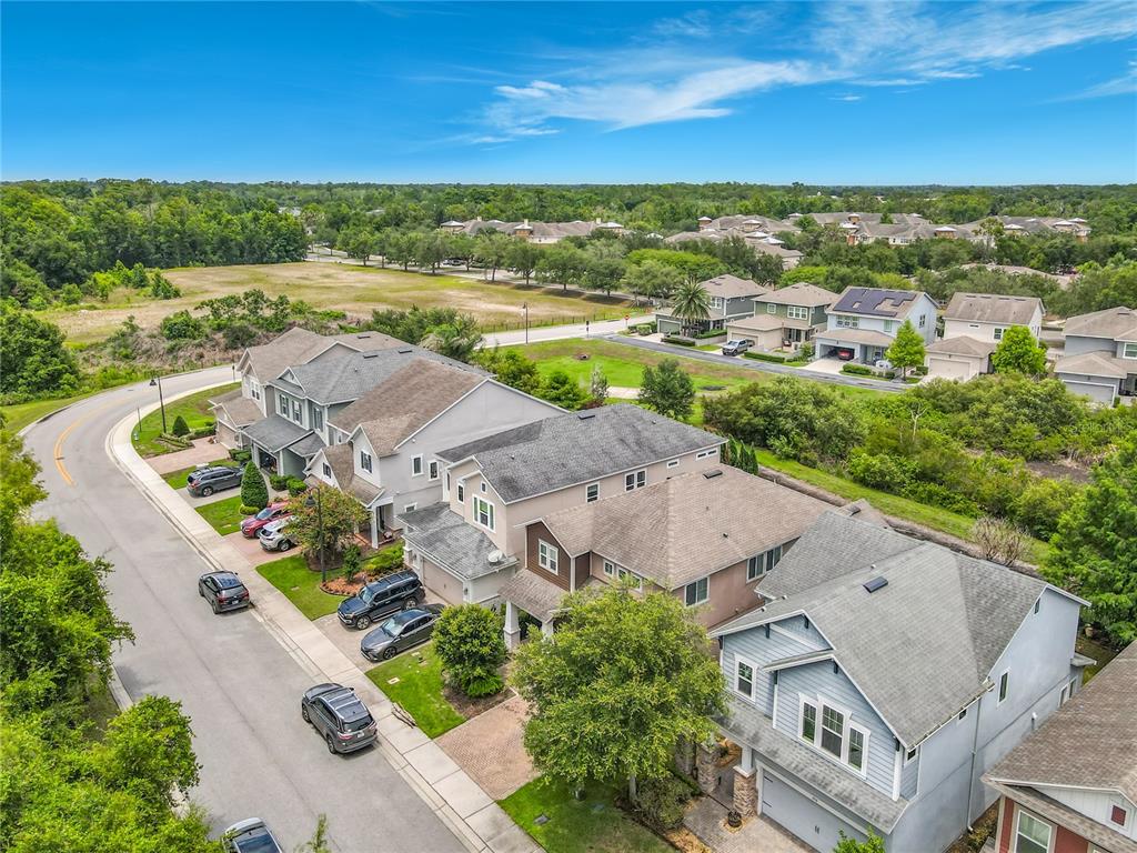 An aerial view shows a suburban street lined with multi-story houses and surrounding green space — 450 WINDY PINE WAY, OVIEDO, FL