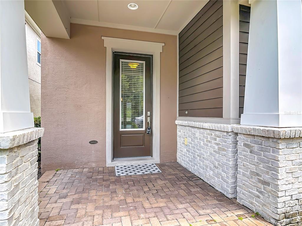 A covered front porch features a brown door, brick pavers, and stone-accented columns — 450 WINDY PINE WAY, OVIEDO, FL