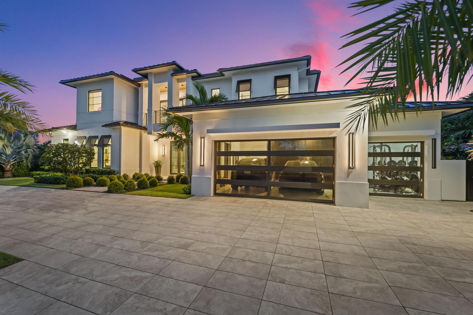 A modern two-story white house features a multi-car garage and a paved driveway at dusk — 830 Lake Shore Drive, Delray Beach FL 33444, DELRAY BEACH, FL
