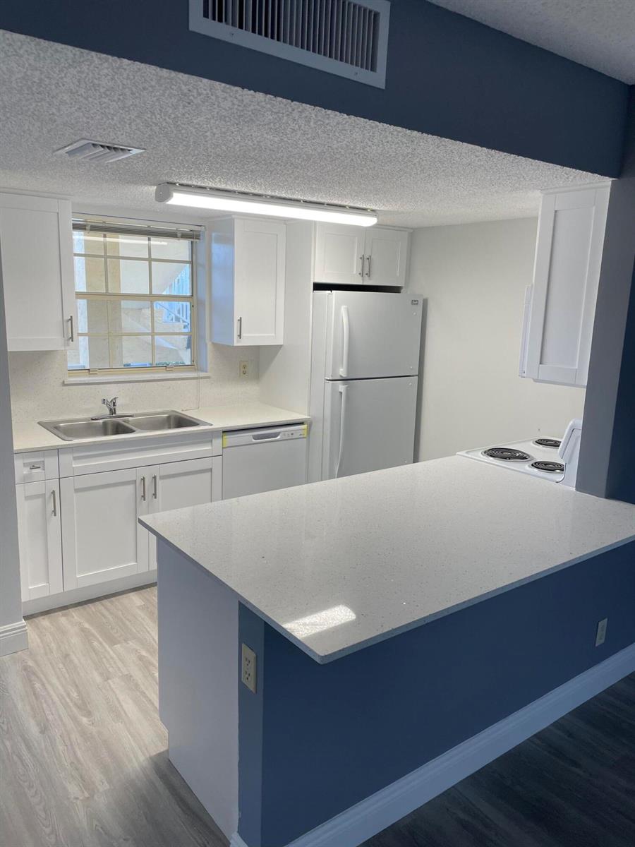 A kitchen features white cabinets, quartz countertops, a double sink, and a white refrigerator — 6284 La Costa Drive # H, Boca Raton FL 33433, BOCA RATON, FL