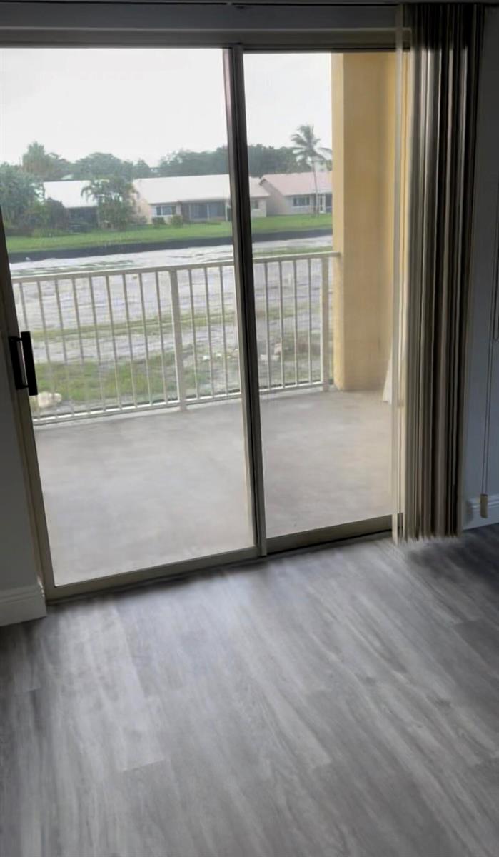 A room with light-colored wood-look flooring features a sliding glass door opening to a balcony — 6284 La Costa Drive # H, Boca Raton FL 33433, BOCA RATON, FL