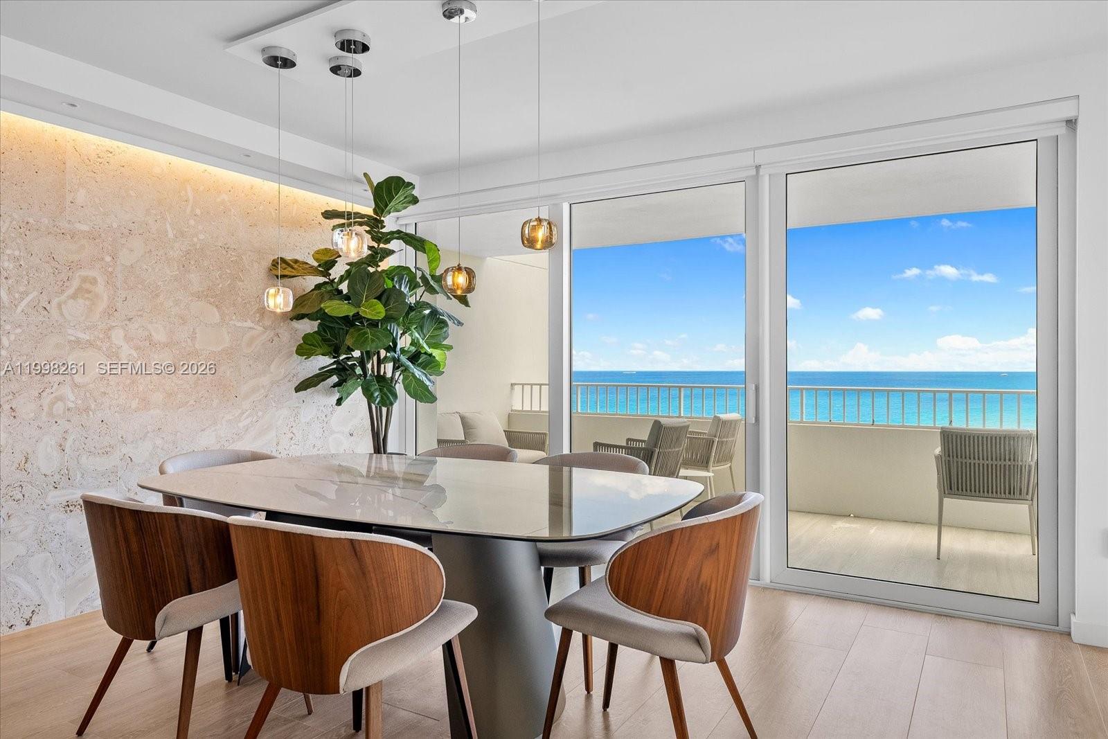 A dining room with a stone accent wall, glass table, and balcony overlooking the ocean — 199 Ocean Lane Dr # 1001, Key Biscayne FL 33149, KEY BISCAYNE, FL