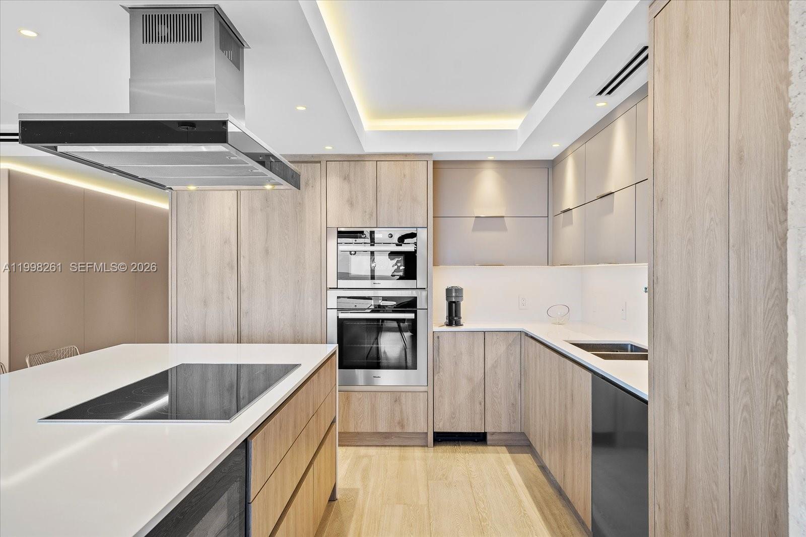 A modern kitchen features light wood cabinetry, white countertops, and a central island with cooktop — 199 Ocean Lane Dr # 1001, Key Biscayne FL 33149, KEY BISCAYNE, FL