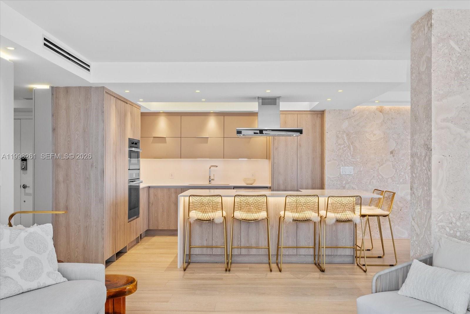A modern kitchen features light wood cabinetry, a stone accent wall, and a central island — 199 Ocean Lane Dr # 1001, Key Biscayne FL 33149, KEY BISCAYNE, FL