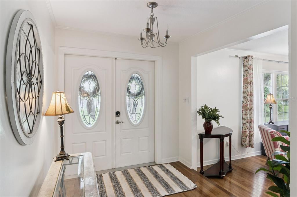 A bright entryway features double front doors, a chandelier, hardwood floors, and a striped rug — 204 BIRCH LANE, LAKELAND, FL