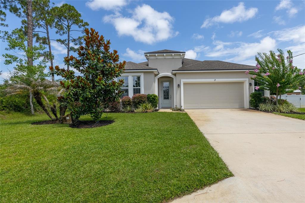 A single-story house with a beige stucco exterior, a two-car garage, and a landscaped lawn — 3 EASTMAN LANE, PALM COAST, FL