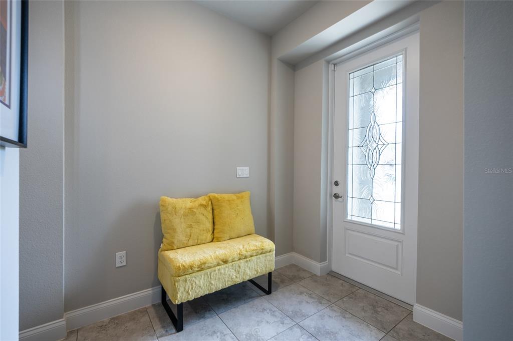 An entryway features a yellow upholstered bench, tiled flooring, and a white front door — 3 EASTMAN LANE, PALM COAST, FL
