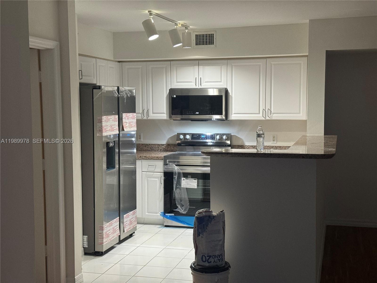 A kitchen features white cabinets, stainless steel appliances, and a granite countertop breakfast bar — 1155 BRICKELL BAY DR # 2309, Miami FL 33131, MIAMI, FL