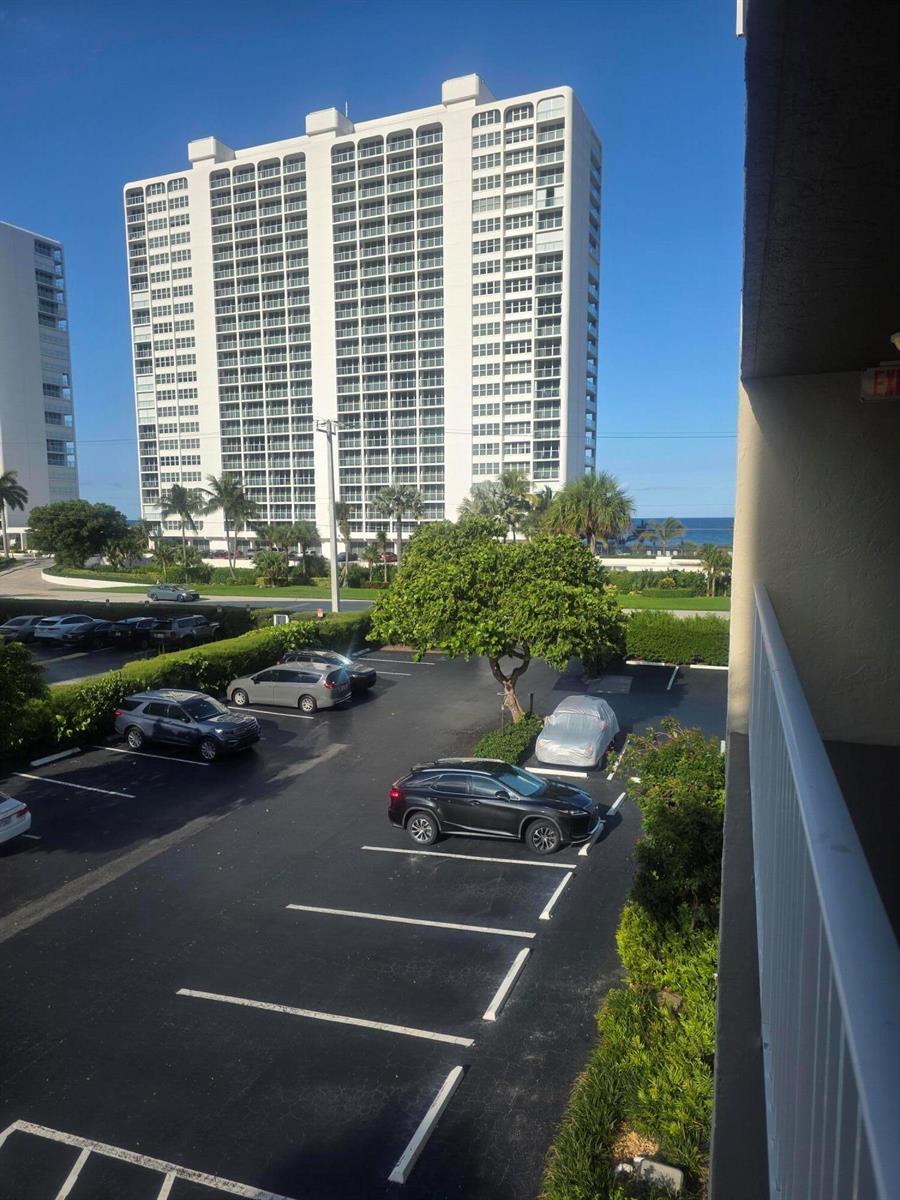 A view from a balcony overlooking a parking lot, palm trees, and a tall building — 2929 S Ocean Boulevard # 5060, Boca Raton FL 33432, BOCA RATON, FL