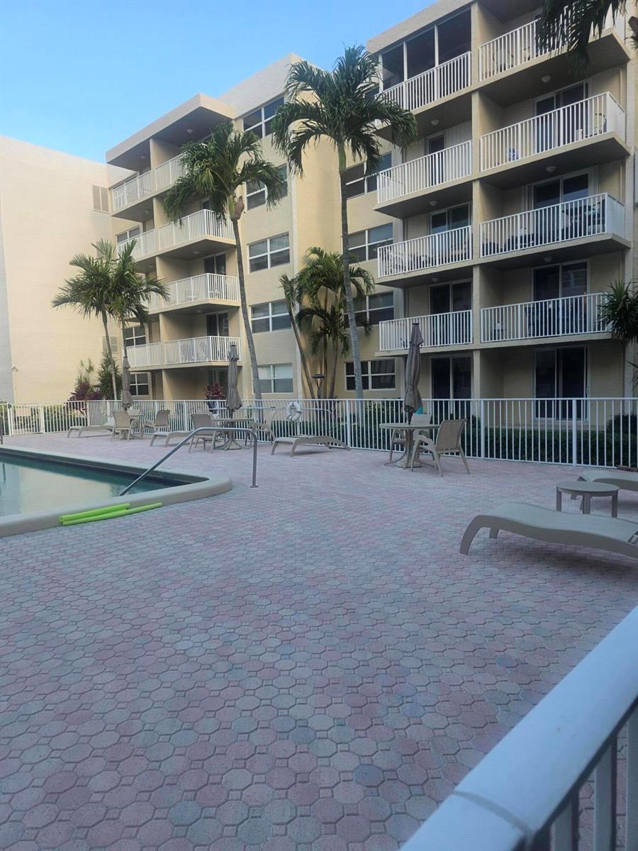 A multi-story apartment building overlooks a paved pool deck with lounge chairs and palm trees — 2929 S Ocean Boulevard # 5060, Boca Raton FL 33432, BOCA RATON, FL
