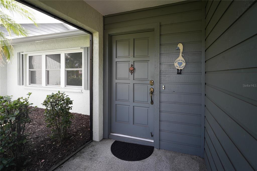 A gray front door with a goose-shaped welcome sign sits on a covered porch — 105 WOODINGHAM DRIVE, VENICE, FL