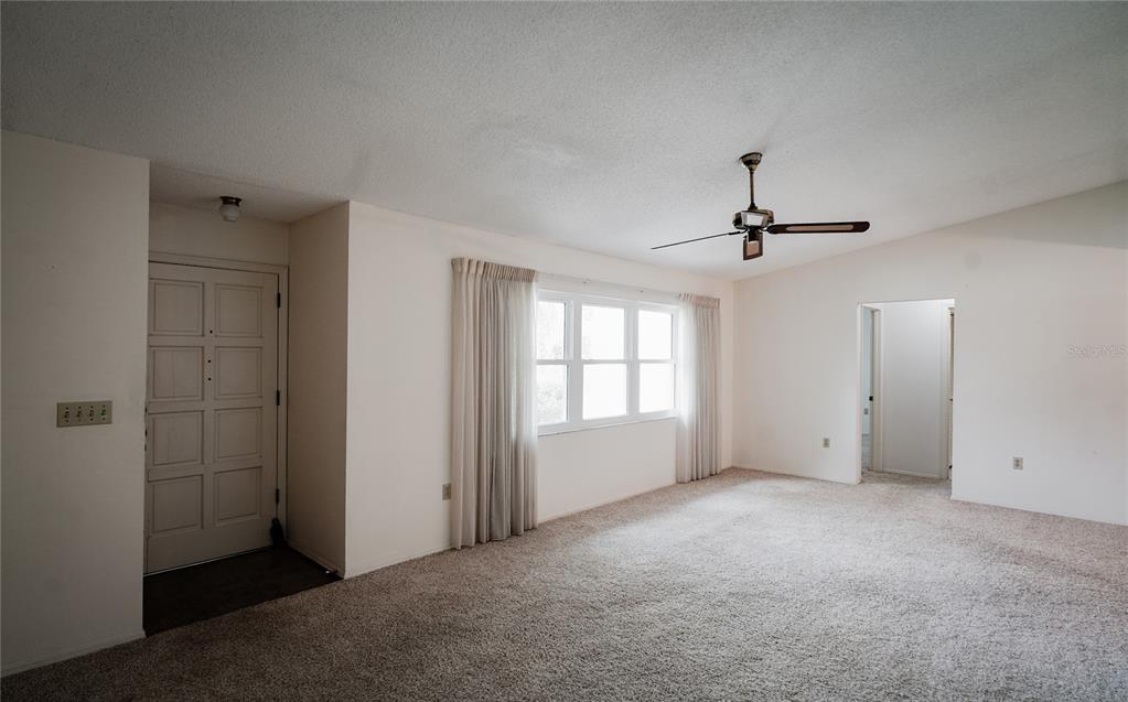 An empty living room features beige carpet, white walls, a ceiling fan, and a front door — 105 WOODINGHAM DRIVE, VENICE, FL