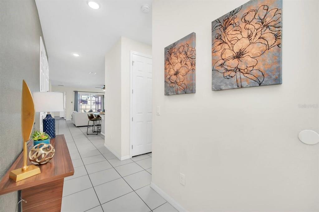 A hallway with tile flooring leads to an open living area with two floral wall canvases — 9009 EGRET MILLS TERRACE, KISSIMMEE, FL