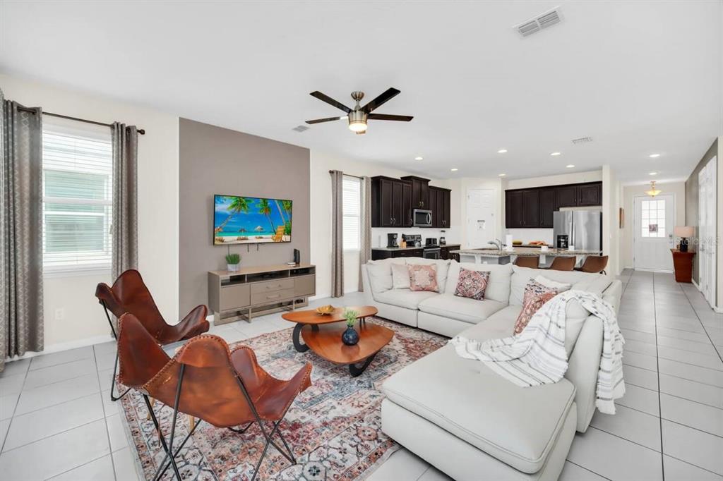 A living room with tile floors, a sectional sofa, two leather chairs, and an open kitchen — 9009 EGRET MILLS TERRACE, KISSIMMEE, FL