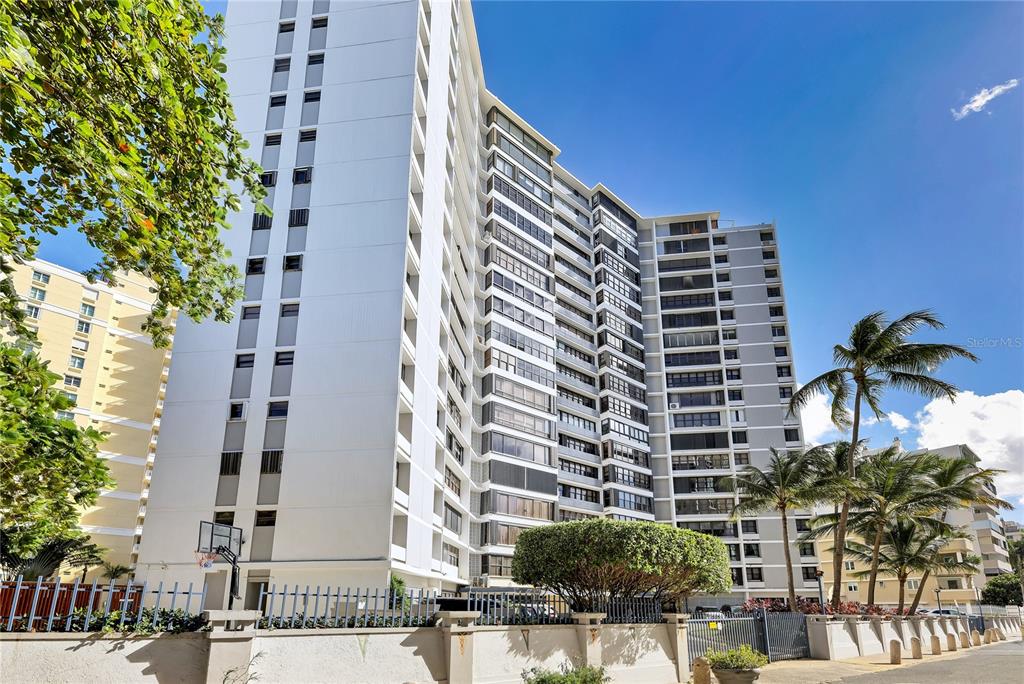A tall, multi-story white apartment building with balconies stands under a clear blue sky — 1 TAFT STREET UNIT PH-C, SAN JUAN, PR