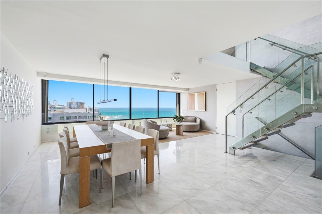 A modern dining room features marble floors, a glass staircase, and floor-to-ceiling ocean views — 1 TAFT STREET UNIT PH-C, SAN JUAN, PR