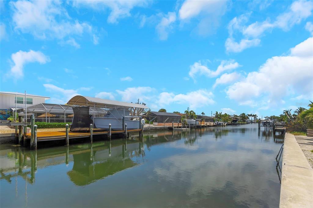 A canal view featuring a boat under a covered lift and residential properties along the banks — 10216 SPOONBILL ROAD E, BRADENTON, FL