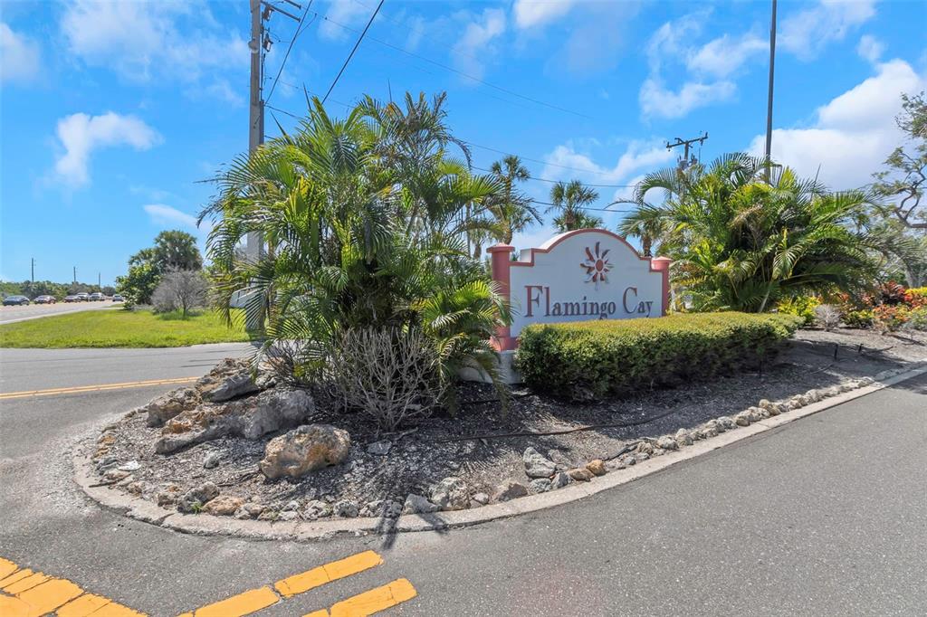 A sign for Flamingo Cay stands in a landscaped island at a road intersection — 10216 SPOONBILL ROAD E, BRADENTON, FL