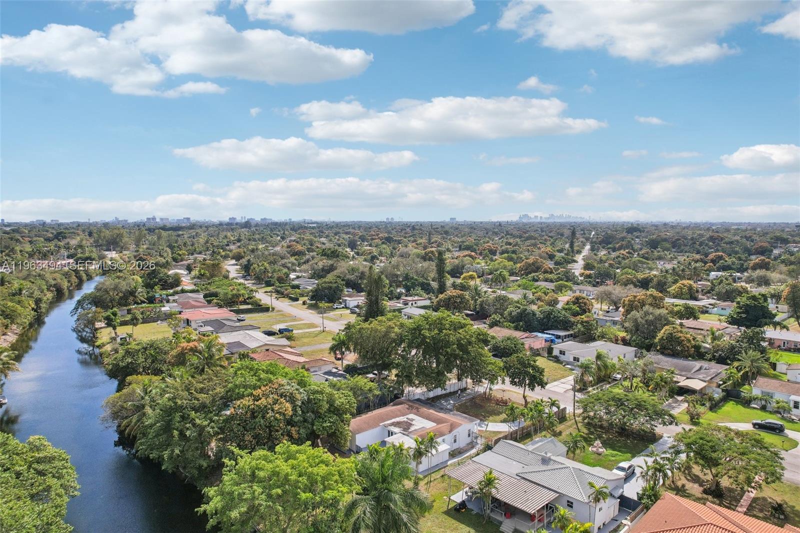An aerial view shows a residential neighborhood with a canal, lush trees, and houses — 299 S Biscayne River Dr, Miami FL 33169, MIAMI, FL